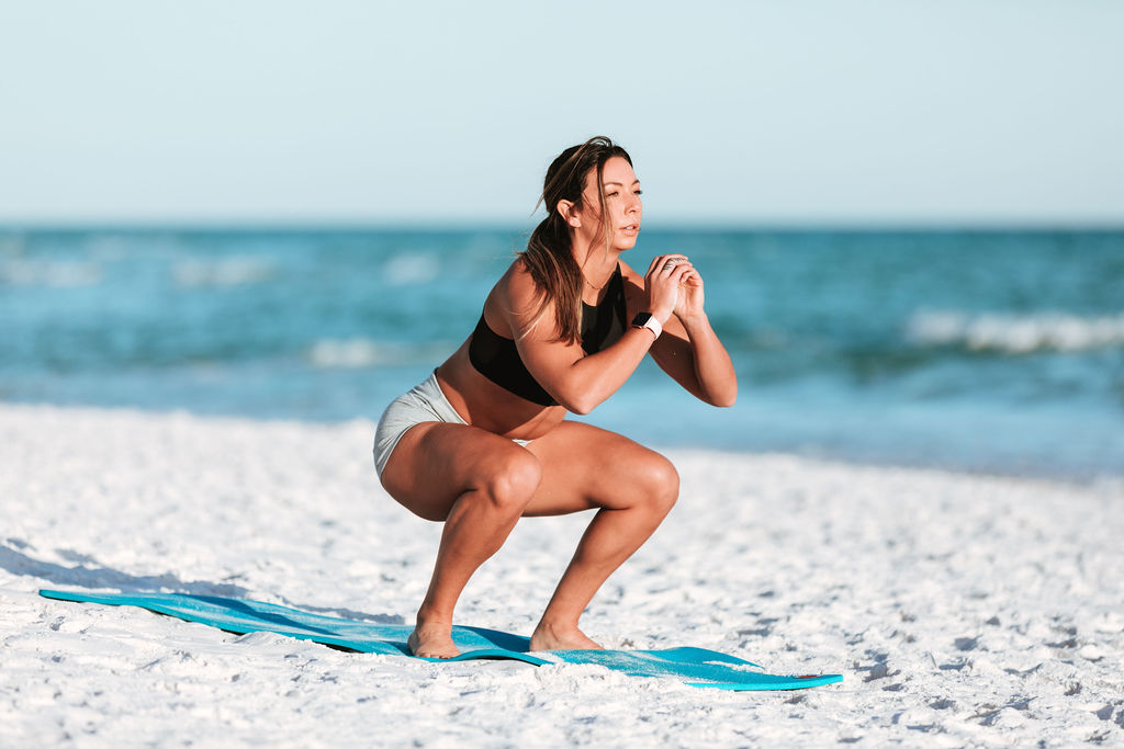 Female Athlete works out at the beach doing squats on a yoga mat in Navarre, Florida during a fitness session.