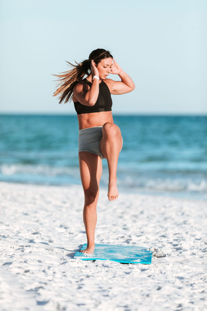 Female Athlete works out at the beach doing squats on a yoga mat in Navarre, Florida during a fitness session.