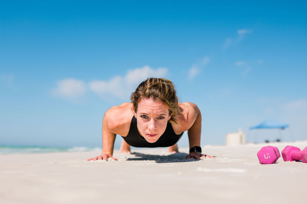 Woman athlete doing plank and pushups on sand during an outdoor female beach fitness photoshoot in Pensacola Beach, Florida. 