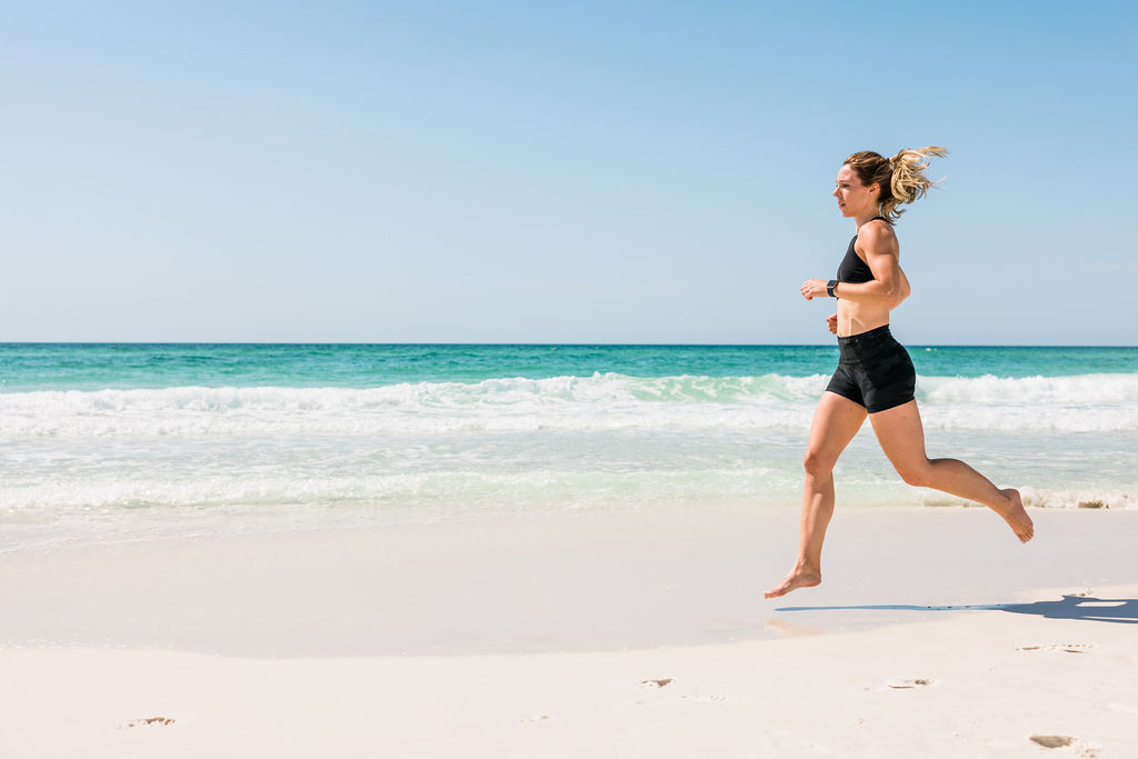 Woman athlete running or jogging on sand during an outdoor female beach fitness photoshoot in Pensacola Beach, Florida. 