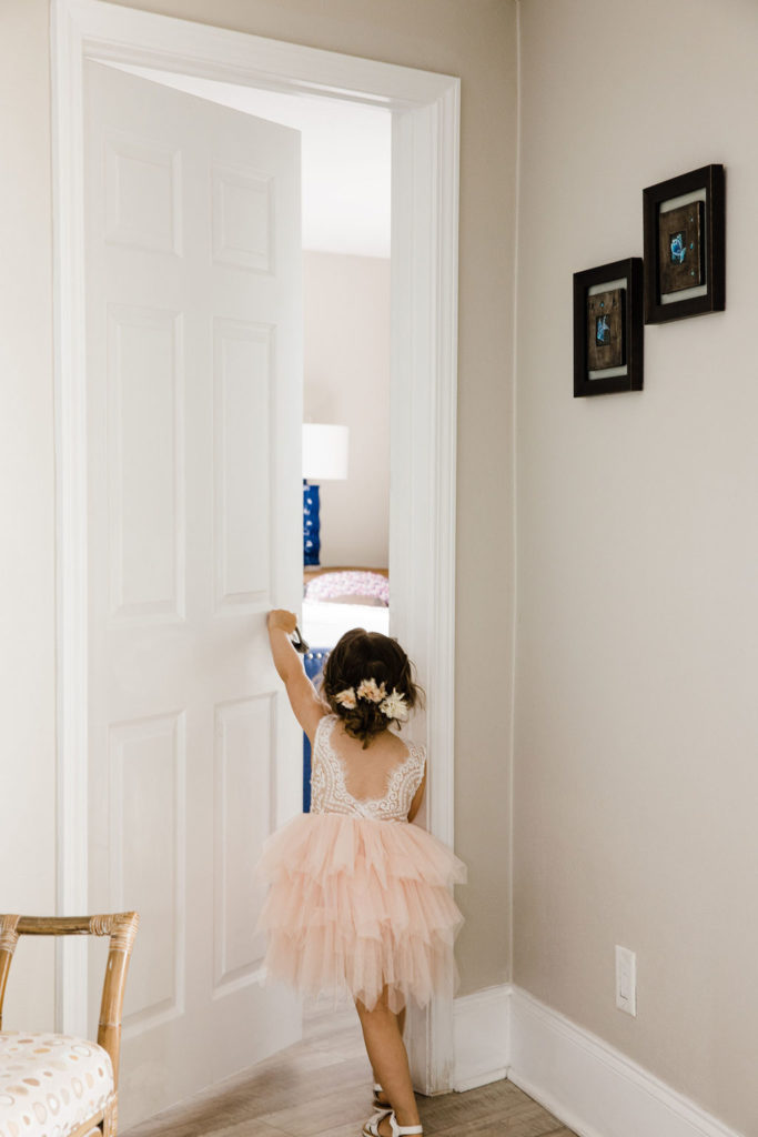 Little girl dressed in wedding attire opens the door to the hotel room for her dad to come out.
