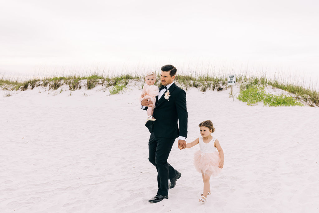 Groom walking down the beach holding his two little girls in Pensacola Beach.