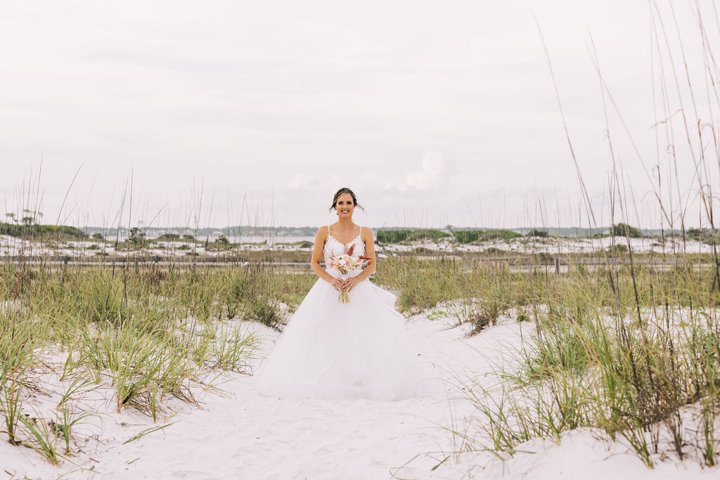 Bride posing in Pensacola Beach on the sand dunes on a cloudy day at sunset before the beach elopement. 