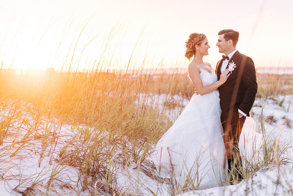Bride and groom standing near the sandy dunes, posing at sunset in Pensacola Beach during their elopement session by Adina.